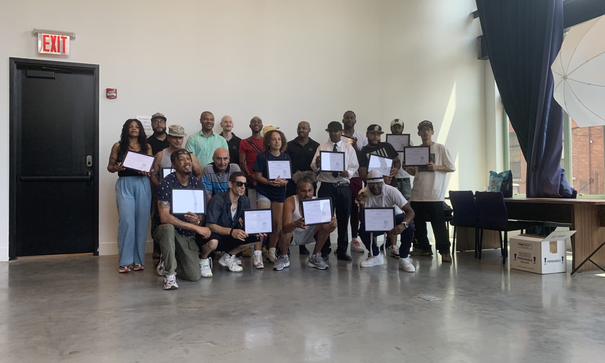 A group of around 20 people poses for a group photo during the graduation ceremony. Many of them hold white certificates in thin black frames.